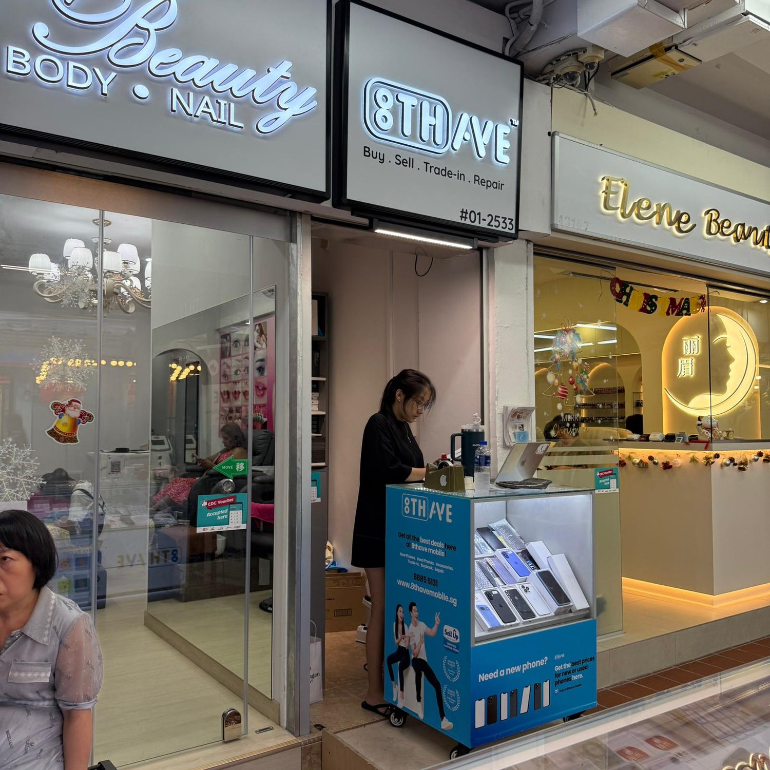 Storefront with '8th Ave' branding and people inside, including a woman using a laptop.